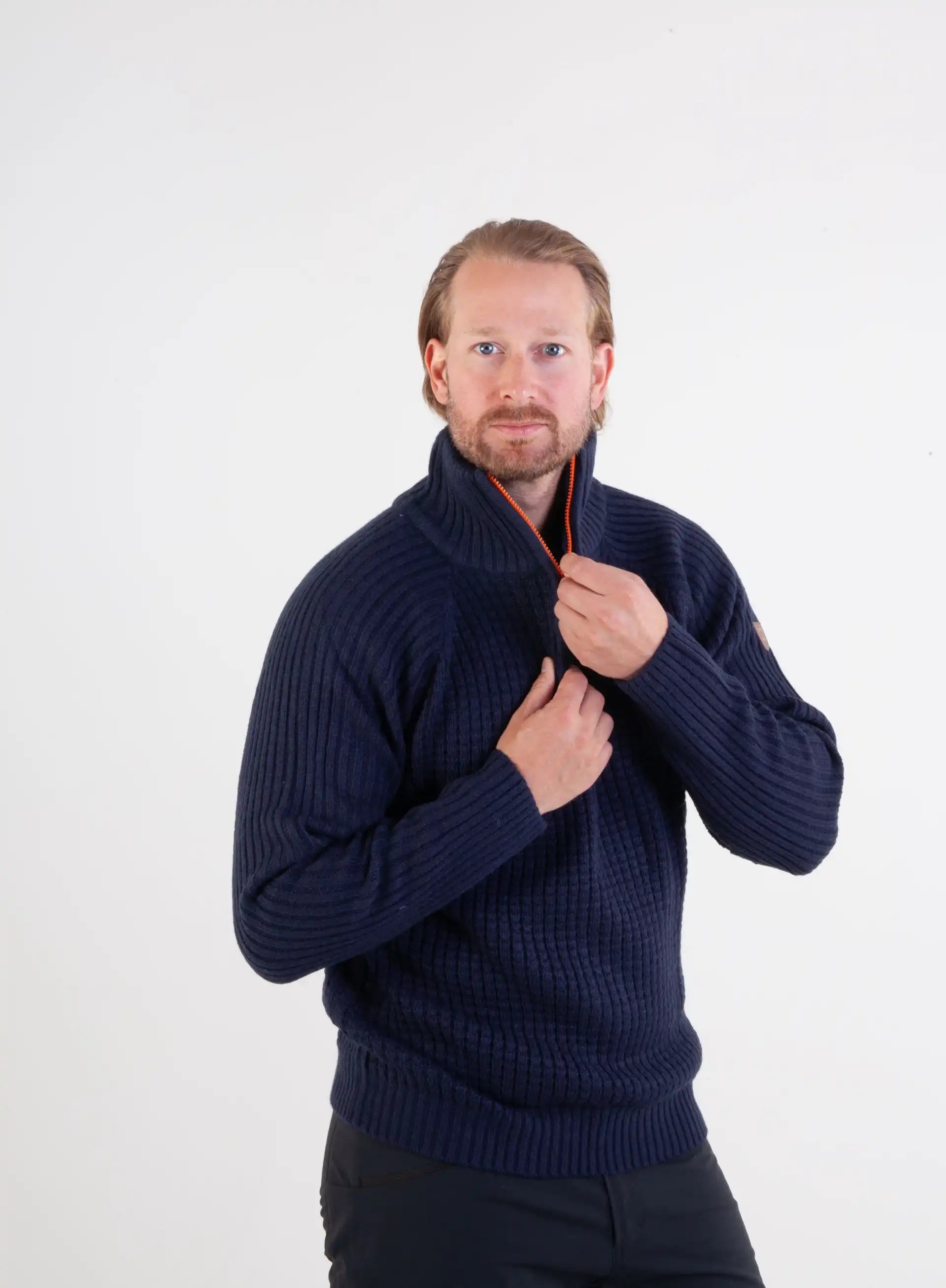 Ullgenser Villmark i blå og orange med høy hals og glidelås, tommelhull for komfort, laget av slitesterk ullblanding, perfekt for friluftsliv og hverdagsbruk.