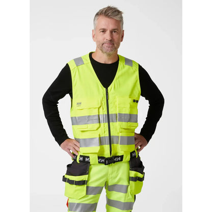 Helly Hansen Alna 2.0 Construction Vest - funksjonell håndverkervest med 2-veis stretchmateriale, forbedret passform, forlengbar front, sømløse refleksbånd for økt sikkerhet, designet for komfort og stil for profesjonelle håndverkere.