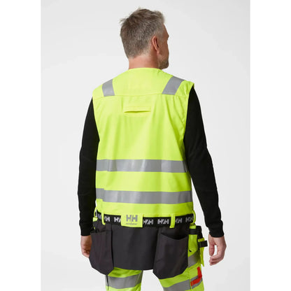 Helly Hansen Alna 2.0 Construction Vest - funksjonell håndverkervest med 2-veis stretchmateriale, forbedret passform, forlengbar front, sømløse refleksbånd for økt sikkerhet, designet for komfort og stil for profesjonelle håndverkere.